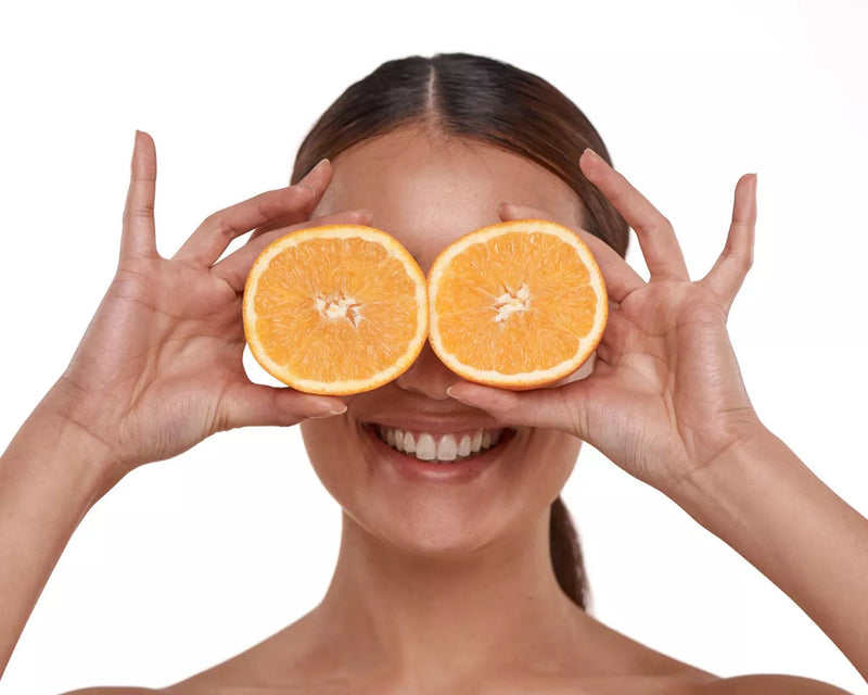 Smiling woman holding orange halves over her eyes against a white background