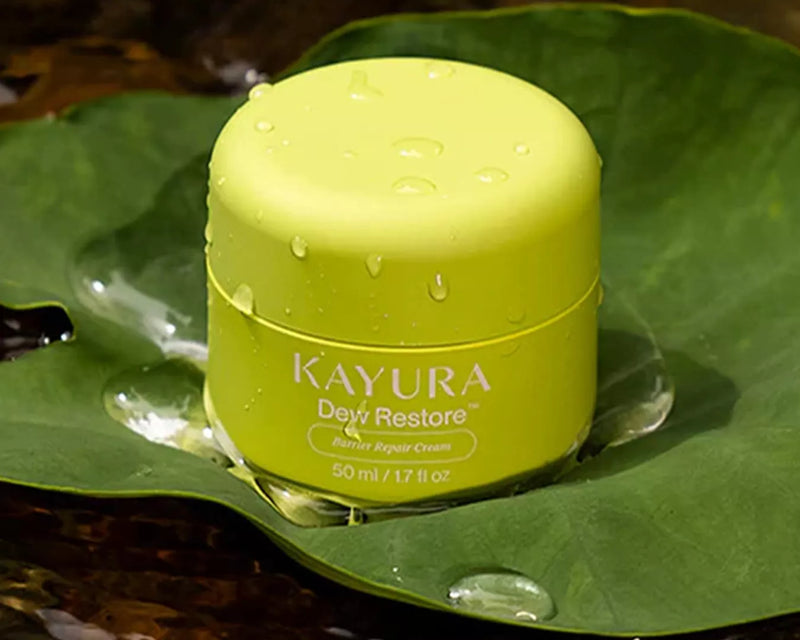 Kayura Dew Restore green moisturiser jar resting on a wet tropical leaf with water droplets