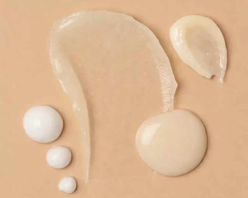 Three droplets of clear and white serum on a warm beige surface