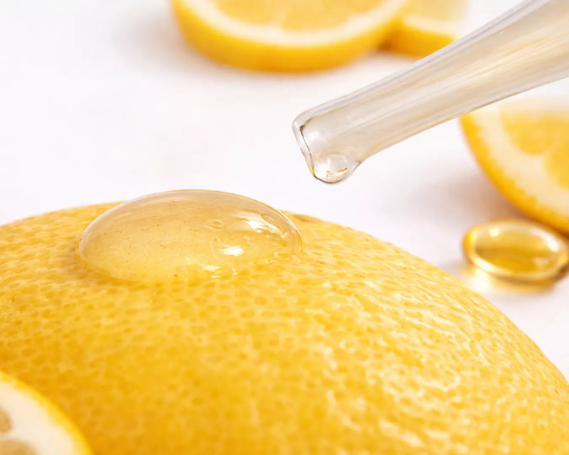 Close-up of a golden serum drop on a lemon surface with a glass dropper, symbolizing Vitamin C